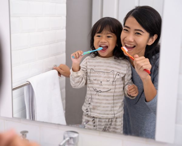 toddler brushing her teeth with her mum