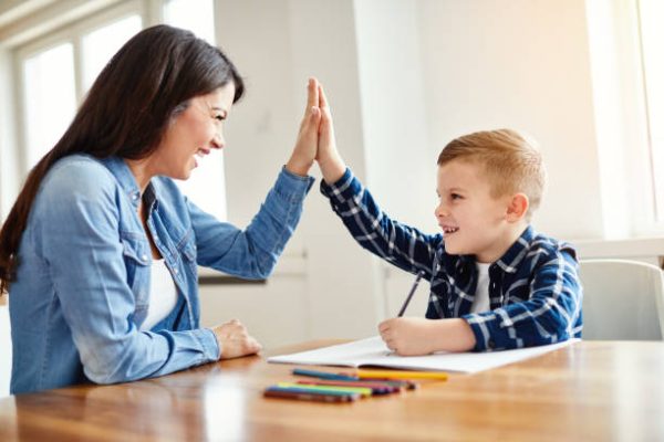 mother teaching son and helping with homework at home, son giving high five to mother