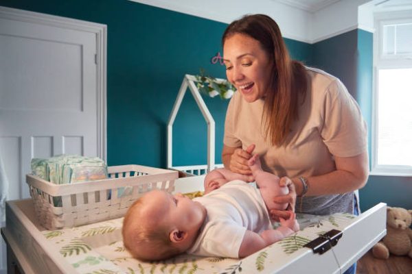 A mother changing her young baby on the changing table in the baby’s room.