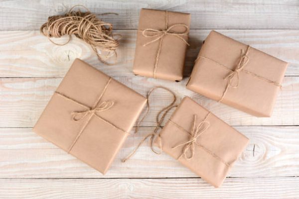 High angle image of four brown packages wrapped with plain brown paper and tied with twine on a white rustic wood table.