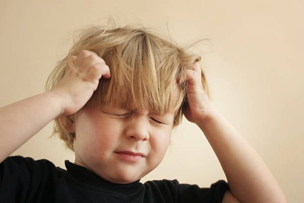A four year old boy scratching his head