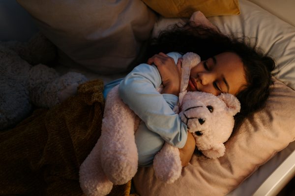 A young boy quietly reads a book in a single bed, tucked under the duvet.